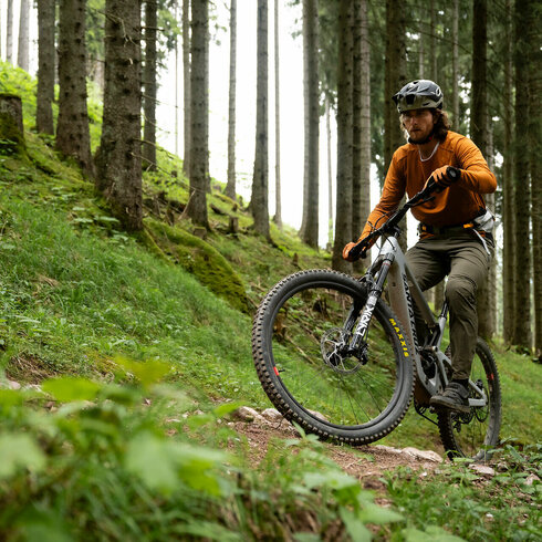 Der Mountainbiker zeigt Geschicklichkeit, während er einen schmalen, bewachsenen Pfad entlangfährt, umgeben von üppiger Natur.