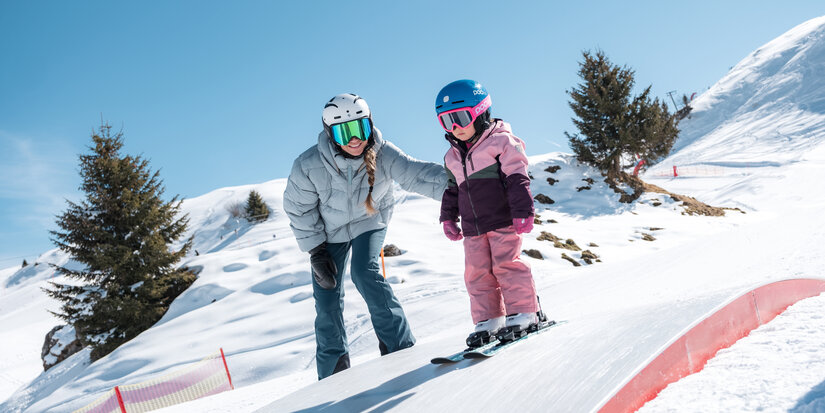 Kind mit Mutter beim Skifahren auf einer Box