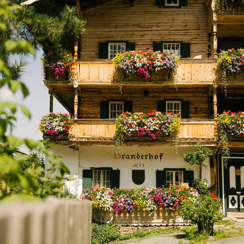 Tradtition Brauchtum Bauernhaus Blumen Details (c) Kitzbuehel Tourismus (1) Ein weißer Flurbereich mit einer offenen Garderobe, Kissen und einem kleinen schwarzen Schild